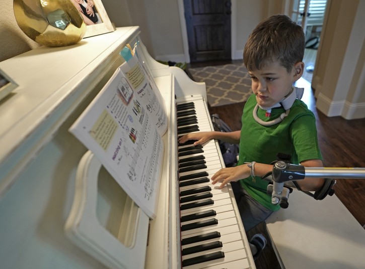Braden Scott uses a device to support his left arm as he practices on the piano in Tomball, Texas on Friday, March 29, 2019. Braden was diagnosed with the syndrome called acute flaccid myelitis, or AFM, in 2016 and was paralyzed almost completely. The rare but mysterious illness seems to ebb and flow every other year and is beginning to alarm public health officials. (AP Photo/David J. Phillip)
