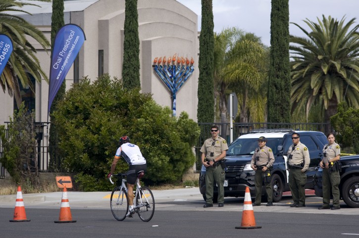 A cyclist rides past several San Diego County Sheriffs who are standing in front of the Chabad of Poway synagogue, background in Poway, California, USA, on 28 April 2019. EPA