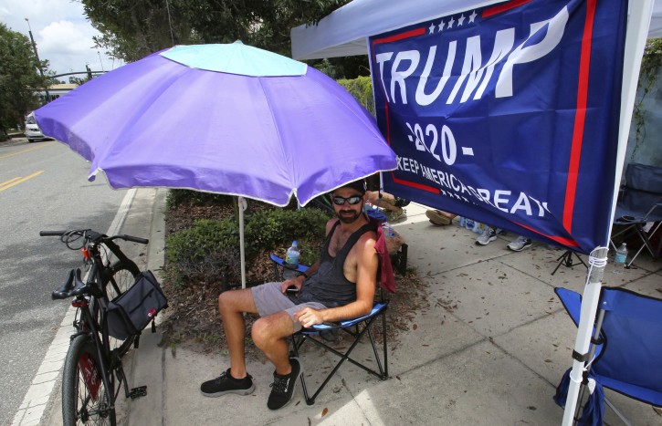 Ray Renaud, from Daytona Beach, Fla., is ready with a beach umbrella as supporters of President Donald Trump camp out in front of the Amway Center, Monday, June 17, 2019, ahead of Tuesday's 2020 campaign kick-off rally in Orlando, Fla. (Joe Burbank/Orlando Sentinel via AP)