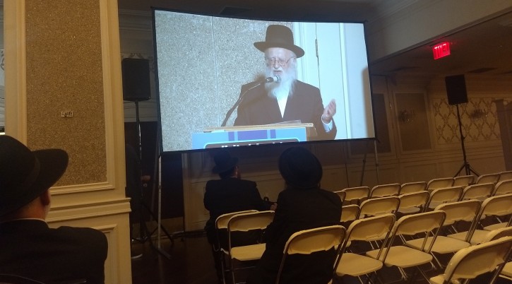 Rabbi Hillel Handler, an Orthodox anti-vaccination leader, speaks via projection screen to an anti-vaccination rally in Brooklyn at a Jewish wedding hall, June 4, 2019. (Ben Sales)