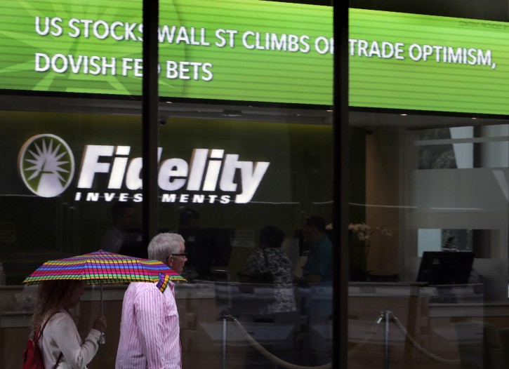 People walk past Fidelity Investments news scroll board, showing a favorable outlook in the US stock markets, in the Financial District of Boston, Tuesday, June 18, 2019.  (AP Photo/Charles Krupa)