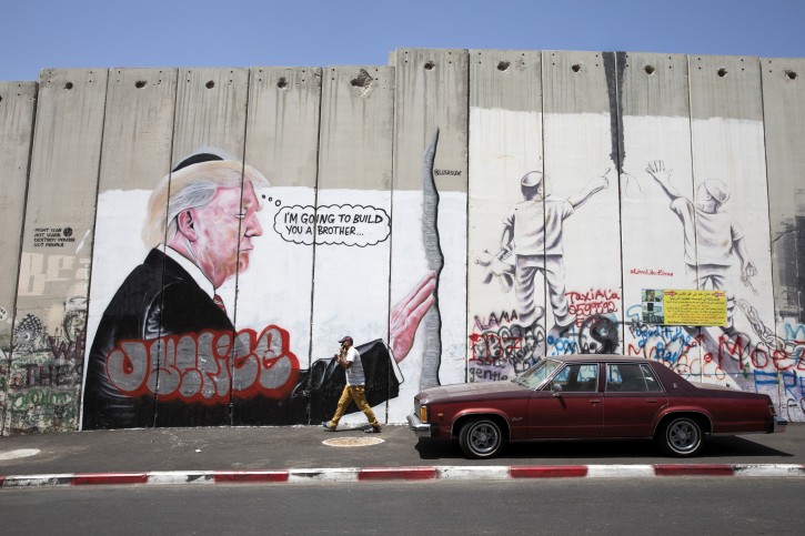  Palestinian man on his cellphone passes a graffiti art work showing US President Donald J. Trump (L) at prayer at the Western Wall in Jerusalem while wearing a yarmulke, or Jewish skull cap, displayed on the controversial Israeli 'separation barrier', or wall, in Bethlehem, West Bank, 27 August 2017. EPA